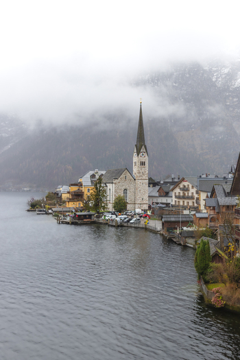 View of the iconic Lutheran Church and traditional alpine houses along the lakefront under misty mountains in Hallstatt Upper Austria Austria. View of the iconic Lutheran Church and traditional alpine houses along the lakefront under misty mountains in Hallstatt Upper Austria Austria.