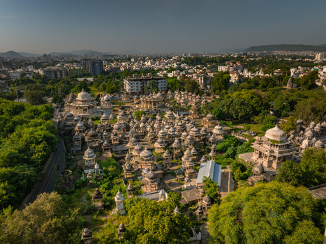 Aerial view of the historic Ahar Cenotaphs with numerous white marble domes surrounded by lush green trees and urban buildings in Udaipur Rajasthan India.