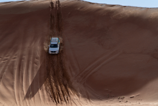 View of a white SUV driving down a steep sand dune with tire tracks in the reddish sand under a clear sky in Dubai Dubai United Arab Emirates. View of a white SUV driving down a steep sand dune with tire tracks in the reddish sand under a clear sky in Dubai Dubai United Arab Emirates.