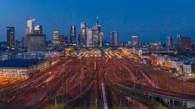 Aerial view of the Hauptbahnhof train station with illuminated tracks and the modern skyline of the financial district at twilight in Frankfurt am Main Hessen Germany.