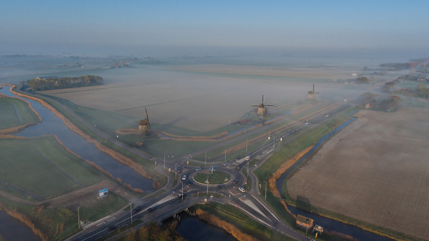 Aerial view of traditional windmills standing along canals and a road roundabout shrouded in morning mist in Schermerhorn North Holland Netherlands. Aerial view of traditional windmills standing along canals and a road roundabout shrouded in morning mist in Schermerhorn North Holland Netherlands.