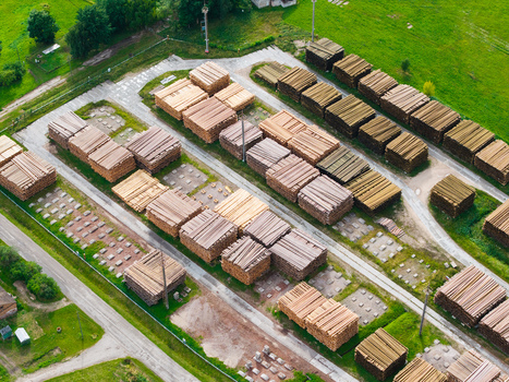 Aerial view of a large timber yard with neatly stacked lumber and logs arranged in rows across a green industrial site in Latvia. Aerial view of a large timber yard with neatly stacked lumber and logs arranged in rows across a green industrial site in Latvia.