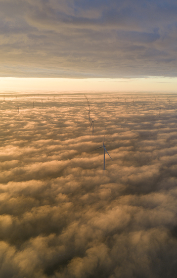 Aerial view of Windpark Fryslan wind turbines emerging from a dense layer of golden clouds at sunset in Breezanddijk Friesland Netherlands.