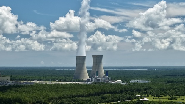 Aerial view of the Seminole Electric Cooperative power plant with cooling towers emitting steam surrounded by dense forests under a bright blue sky in Palatka Florida United States.