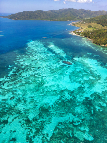 Aerial view of the vibrant turquoise coral reefs and lush green hills along the tropical coastline Guanaja Bay Islands Department Honduras. Aerial view of the vibrant turquoise coral reefs and lush green hills along the tropical coastline Guanaja Bay Islands Department Honduras.