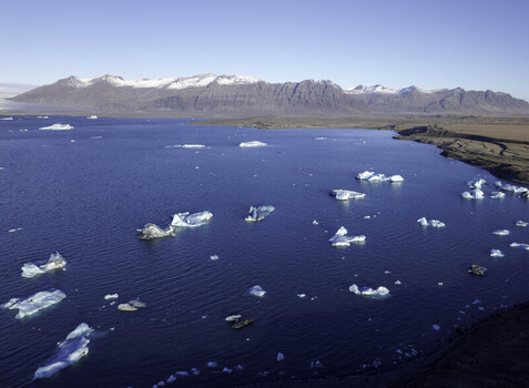 Aerial view of Jokulsarlon Glacier Lagoon with floating icebergs in the deep blue water surrounded by snow capped mountains under a clear sky in Iceland. Aerial view of Jokulsarlon Glacier Lagoon with floating icebergs in the deep blue water surrounded by snow capped mountains under a clear sky in Iceland.