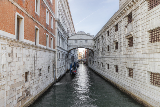 View of the historic Bridge of Sighs spanning a narrow canal with a gondola passing underneath surrounded by ornate stone architecture in Venice Veneto Italy. View of the historic Bridge of Sighs spanning a narrow canal with a gondola passing underneath surrounded by ornate stone architecture in Venice Veneto Italy.