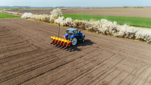 Aerial view of a blue tractor working the dark soil contrasts with the bright white blossoms lining the field s edge Sremska Mitrovica Vojvodina Serbia. Aerial view of a blue tractor working the dark soil contrasts with the bright white blossoms lining the field s edge Sremska Mitrovica Vojvodina Serbia.
