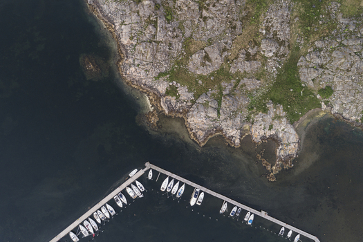 Aerial view of Sando marina with docked sailboats along a wooden pier rocky coastline and dark water in Vallda Hallands lan Sweden.