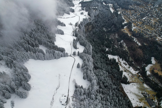 Aerial view of Les Rives area featuring snow covered alpine meadows dense pine forests and a steep cliff edge under misty clouds in Champery Valais Switzerland.