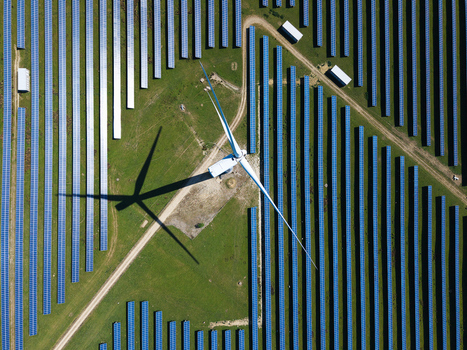Aerial view of Chelveston Wind Farm with a large wind turbine casting a shadow over rows of blue solar panels on green fields in Wellingborough England United Kingdom. Aerial view of Chelveston Wind Farm with a large wind turbine casting a shadow over rows of blue solar panels on green fields in Wellingborough England United Kingdom.
