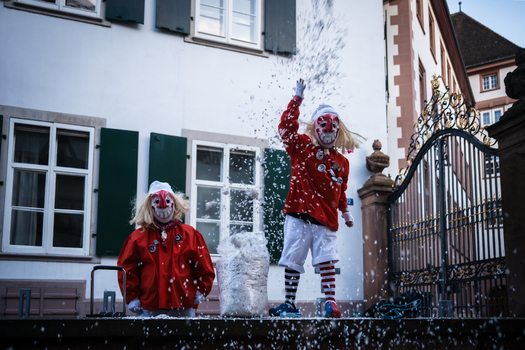 Basel Switzerland 10 March 2025 View of two masked figures in red and white costumes playfully throwing confetti against a backdrop of classic architecture.. Basel Switzerland 10 March 2025 View of two masked figures in red and white costumes playfully throwing confetti against a backdrop of classic architecture..