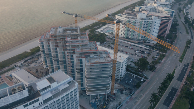 Aerial view of a high rise building under construction with tall cranes situated along the coast with nearby hotels and roads in Miami Beach Florida United States. Aerial view of a high rise building under construction with tall cranes situated along the coast with nearby hotels and roads in Miami Beach Florida United States.