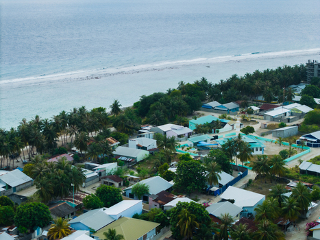 Aerial view of turquoise waters meet the sandy shore embracing the vibrant hues of homes nestled amidst lush greenery Vashafaru Island Thiladhummathi Atoll Maldives. Aerial view of turquoise waters meet the sandy shore embracing the vibrant hues of homes nestled amidst lush greenery Vashafaru Island Thiladhummathi Atoll Maldives.