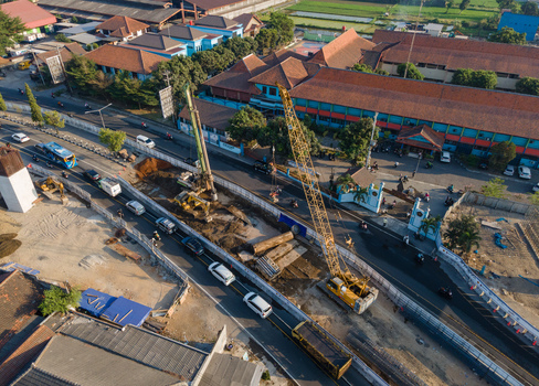 Aerial view of a road construction site with a large yellow crane and excavators operating near traffic in an urban area of Yogyakarta Special Region of Yogyakarta Indonesia. Aerial view of a road construction site with a large yellow crane and excavators operating near traffic in an urban area of Yogyakarta Special Region of Yogyakarta Indonesia.