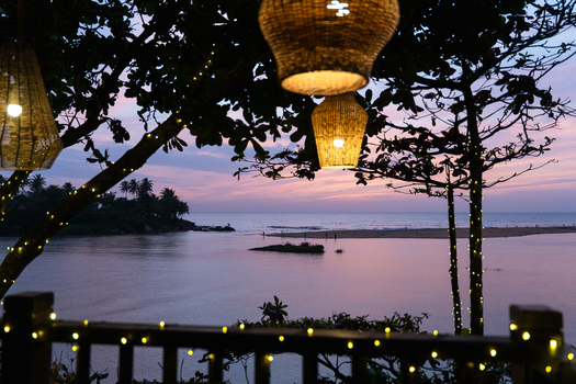 View of a tranquil bay at sunset through trees decorated with fairy lights and wicker lamps in Galle Southern Province Sri Lanka.