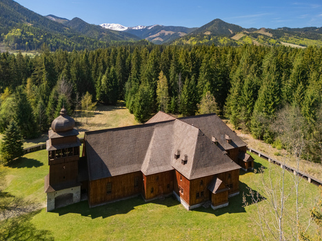 Aerial view of the Wooden Articular Church of Svaty Kriz surrounded by a dense evergreen forest and snow capped mountains in Svaty Kriz Zilinsky kraj Slovakia.