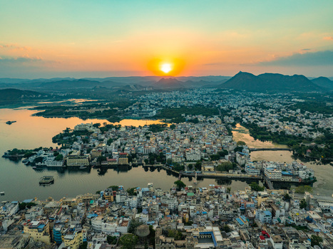 Aerial view of the historic city of Udaipur at sunset featuring the architecture and buildings surrounding the serene Lake Pichola in Udaipur Rajasthan India.