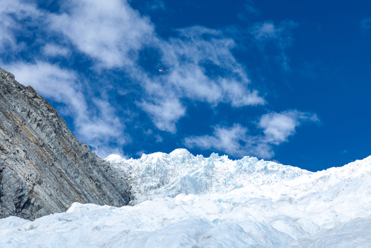 View of a dazzling white glacier cascading down a rugged mountain under a brilliant blue sky dotted with fluffy clouds Franz Josef Glacier West Coast Region New Zealand. View of a dazzling white glacier cascading down a rugged mountain under a brilliant blue sky dotted with fluffy clouds Franz Josef Glacier West Coast Region New Zealand.