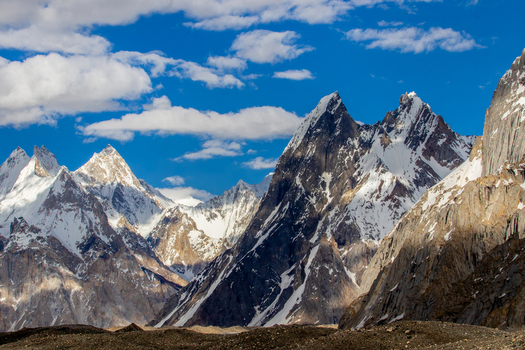 View of the snow capped peaks of Mango Gusor mountain under a blue sky with white clouds in Skardu Gilgit Pakistan.