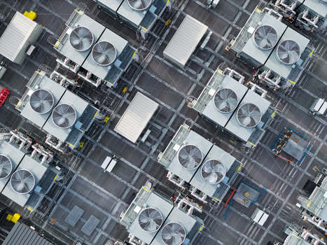 Aerial view of a data center roof featuring a grid of industrial cooling fans and HVAC units in the United Kingdom. Aerial view of a data center roof featuring a grid of industrial cooling fans and HVAC units in the United Kingdom.