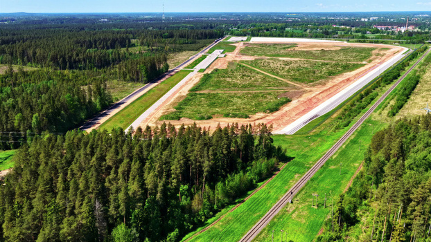 Aerial view of a large cleared construction site surrounded by dense pine forests and a railway line running alongside the green landscape in Latvija. Aerial view of a large cleared construction site surrounded by dense pine forests and a railway line running alongside the green landscape in Latvija.