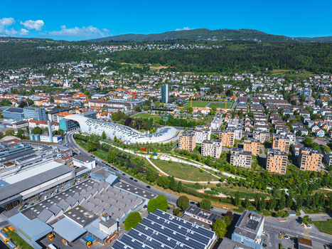 Aerial view of the modern Swatch Omega Campus building with its unique curved architecture surrounded by urban greenery and forested hills in Biel Bienne Canton of Bern Switzerland.