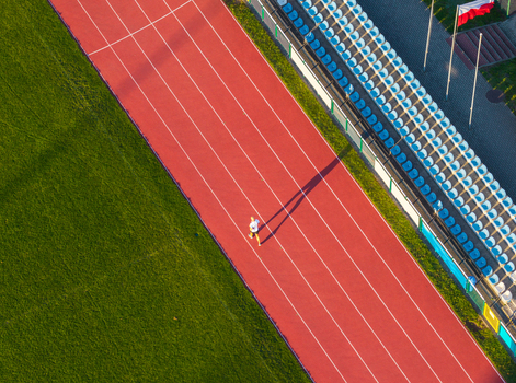 Aerial view of the Sports and Recreation Center with a red running track green grass and blue stadium seating with a runner in Starogard Gdanski Pomeranian Voivodeship Poland. Aerial view of the Sports and Recreation Center with a red running track green grass and blue stadium seating with a runner in Starogard Gdanski Pomeranian Voivodeship Poland.