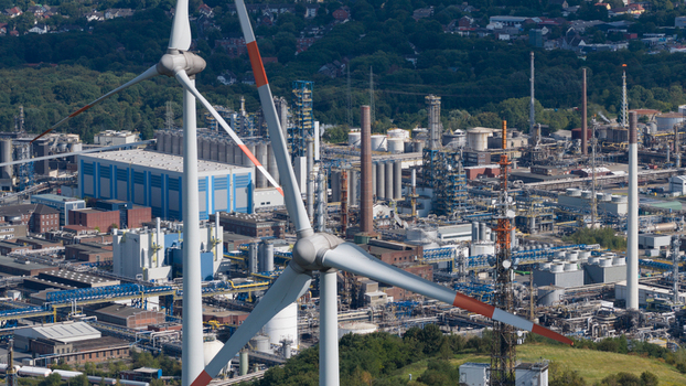 Aerial view of a wind turbine in the foreground with an industrial tank farm and refinery complex in the background in Gelsenkirchen North Rhine Westphalia Germany.