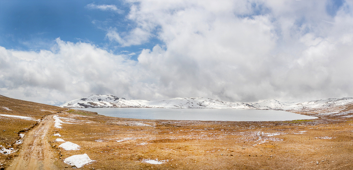 View of Sheosar Lake surrounded by snow capped mountains and a dirt road under a cloudy sky in Skardu Gilgit Pakistan. View of Sheosar Lake surrounded by snow capped mountains and a dirt road under a cloudy sky in Skardu Gilgit Pakistan.