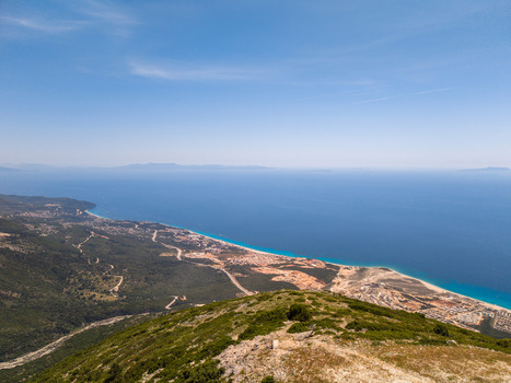 Aerial view of the turquoise coastline and sandy beach with green hills and construction sites under a clear blue sky in Palase Vlore County Albania.