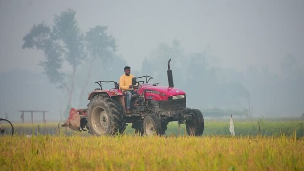 View of a man driving a red tractor in a field Bangladesh.