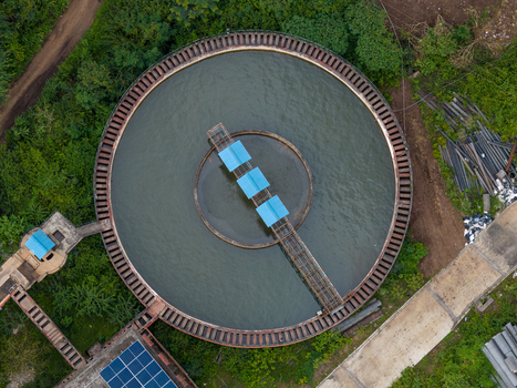 Aerial view of a circular water treatment clarifier tank with a central bridge and blue roof structures surrounded by greenery and industrial infrastructure in Karad Maharashtra India.