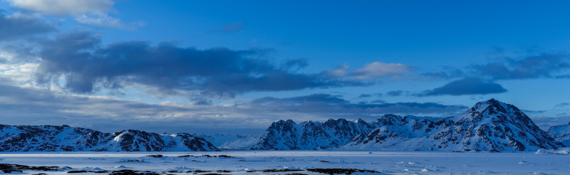 Aerial view of snow capped mountain ranges and a vast frozen fjord under a deep blue sky with soft clouds Tasiilaq Sermersooq Greenland. Aerial view of snow capped mountain ranges and a vast frozen fjord under a deep blue sky with soft clouds Tasiilaq Sermersooq Greenland.