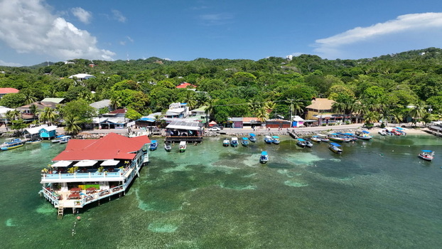 Aerial view of West End with overwater restaurants boats in clear turquoise water and lush tropical vegetation on the hillside in West End Bay Islands Department Honduras. Aerial view of West End with overwater restaurants boats in clear turquoise water and lush tropical vegetation on the hillside in West End Bay Islands Department Honduras.