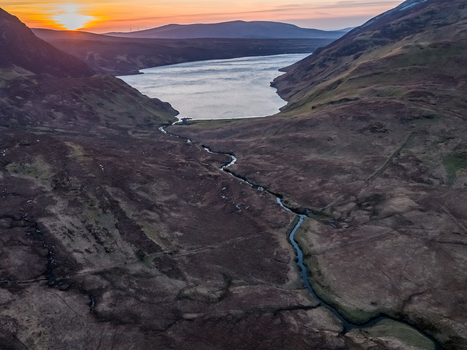 Aerial view of Altan Lough surrounded by rugged hills and a winding stream at sunset in County Donegal Ireland.