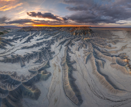 Aerial view of the dramatic badlands landscape with deep erosion patterns and ridges under a vibrant sunset sky in Hanksville Utah United States.