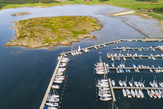 Aerial view of Sando marina with numerous sailboats docked in rows along wooden piers surrounded by calm blue water and green coastal landscape in Vallda Hallands lan Sweden.