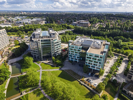 Aerial view of modern office buildings along Lakeside Drive surrounded by lush green parkland a small canal and suburban trees in London England United Kingdom. Aerial view of modern office buildings along Lakeside Drive surrounded by lush green parkland a small canal and suburban trees in London England United Kingdom.