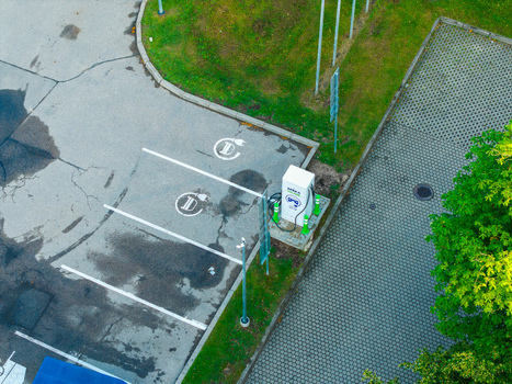 Aerial view of an electric vehicle charging station in a parking lot with puddles on the asphalt and surrounding green grass in Riga Latvia.