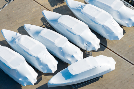 Aerial view of several motorboats wrapped in white protective plastic covers at an advanced motorboat production facility in Poland.