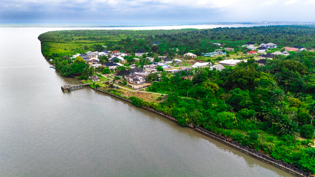 Aerial view of a coastal settlement nestled along a riverbank featuring residential houses lush green vegetation and a small pier extending into the water in Minima Rivers Nigeria.