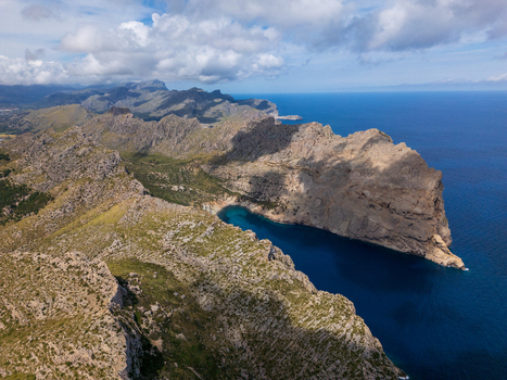 Aerial view of Cap de Formentor with rugged limestone cliffs deep blue Mediterranean sea and rocky mountain ridges under a cloudy sky Balearic Islands Spain.