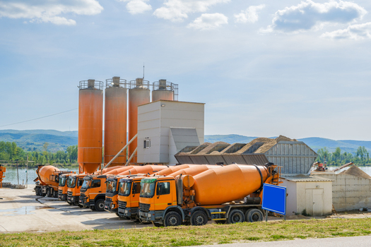 View of orange concrete mixer trucks parked at an industrial facility with silos and distant hills in Novi Sad Vojvodina Serbia. View of orange concrete mixer trucks parked at an industrial facility with silos and distant hills in Novi Sad Vojvodina Serbia.