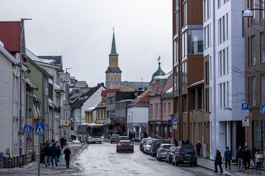 Tromso Norway 07 March 2026 View of a city street with the Tromso Cathedral spire in the background featuring pedestrians a bus and a mix of modern and old architecture. Tromso Norway 07 March 2026 View of a city street with the Tromso Cathedral spire in the background featuring pedestrians a bus and a mix of modern and old architecture.