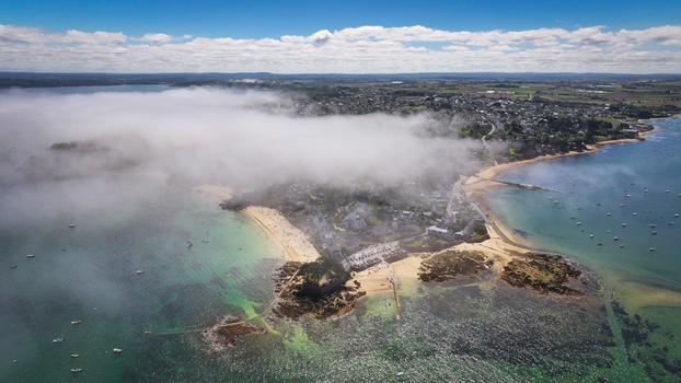 Aerial view of a coastal town shrouded in ethereal mist where the emerald sea meets the sandy shore Carantec Bretagne France.