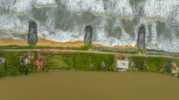 Aerial view of Mattu Beach featuring stone breakwaters extending into the sea sandy coastline and a road separating the beach from the backwaters in Udupi Karnataka India.