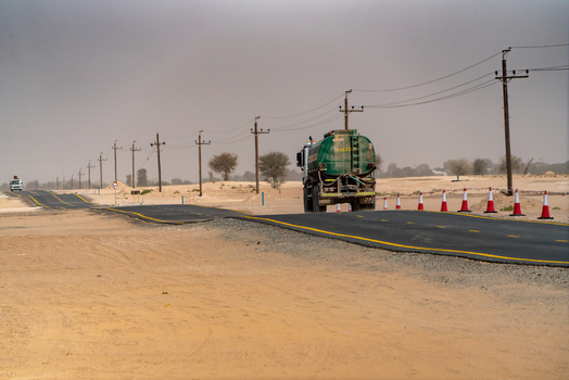 View of a green water tanker truck driving on a newly paved asphalt road through the desert landscape with utility poles and traffic cones Dubai Dubai United Arab Emirates. View of a green water tanker truck driving on a newly paved asphalt road through the desert landscape with utility poles and traffic cones Dubai Dubai United Arab Emirates.