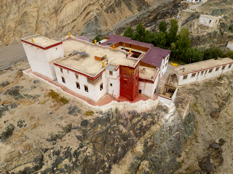 Aerial view of the historic Zanskar monastery perched on a rocky cliff featuring traditional white and red walls flat rooftops and arid mountain landscape in Zanskar Ladakh India.