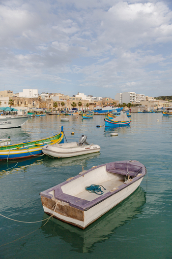 View of colorful boats bobbing gently on the turquoise water reflecting the sky with the town s buildings in the background Marsaxlokk Malta. View of colorful boats bobbing gently on the turquoise water reflecting the sky with the town s buildings in the background Marsaxlokk Malta.